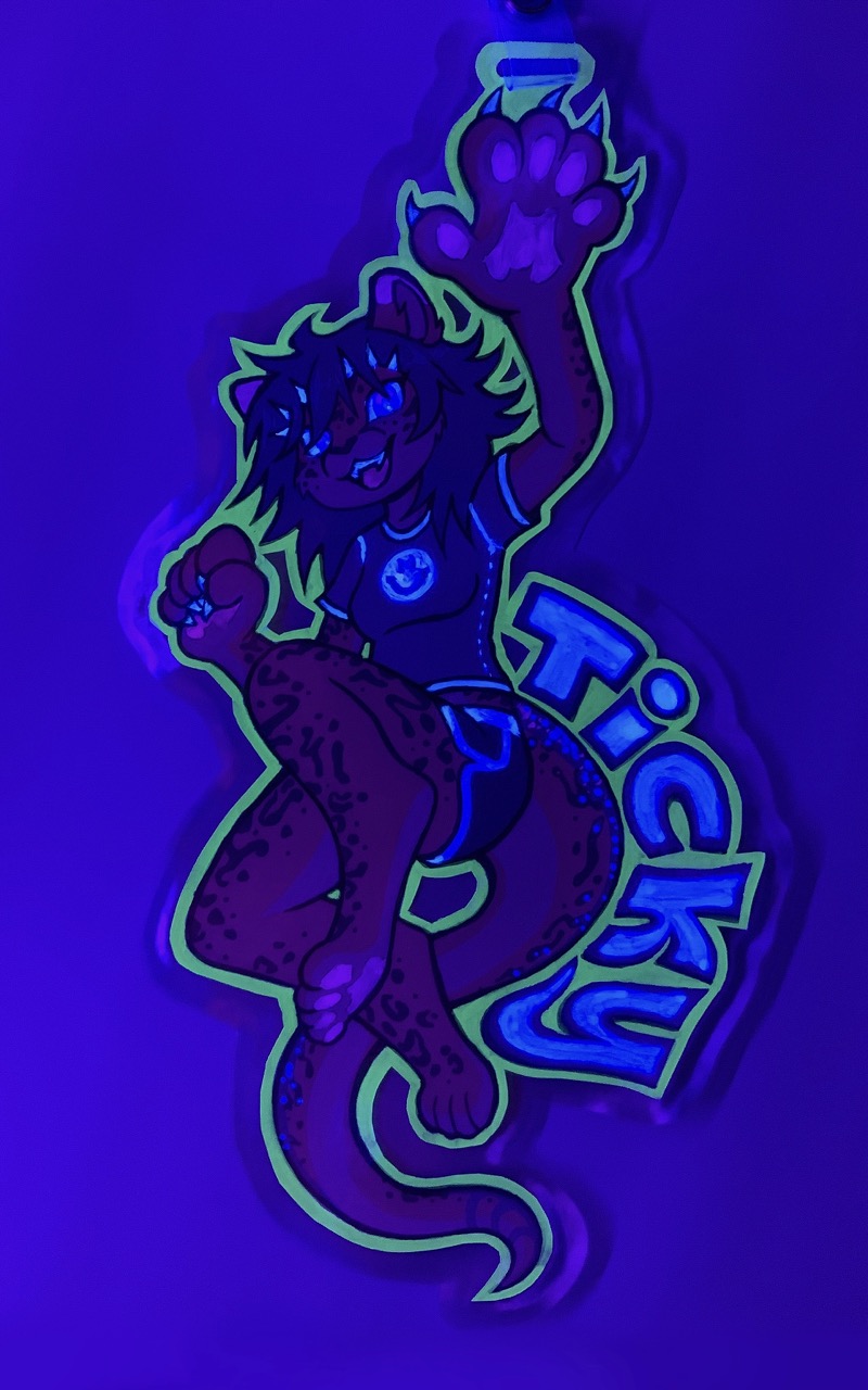 The same badge as above, but under ultraviolet light; the border fluoresces a delightful yellow-green, Ticky's claws, teeth, and scales glow a little more white, and the name glows pleasantly also
